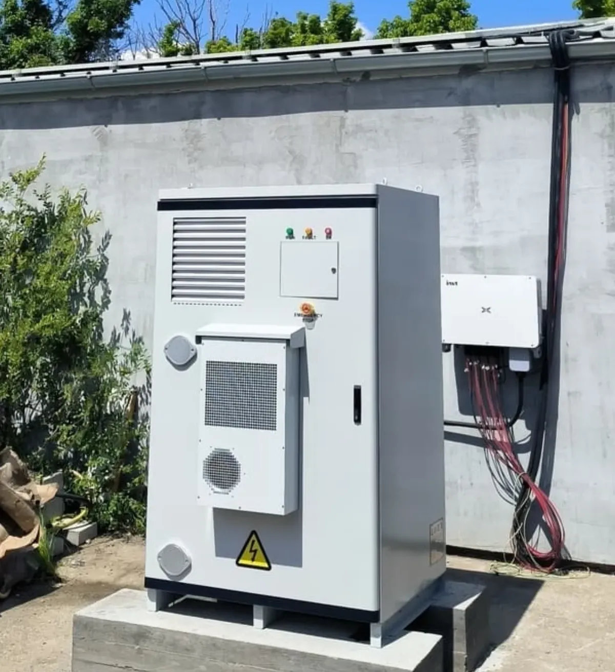Air-cooled storage cabinet on an outdoor concrete pad beside existing wall-mounted conversion and distribution equipment at a commercial site