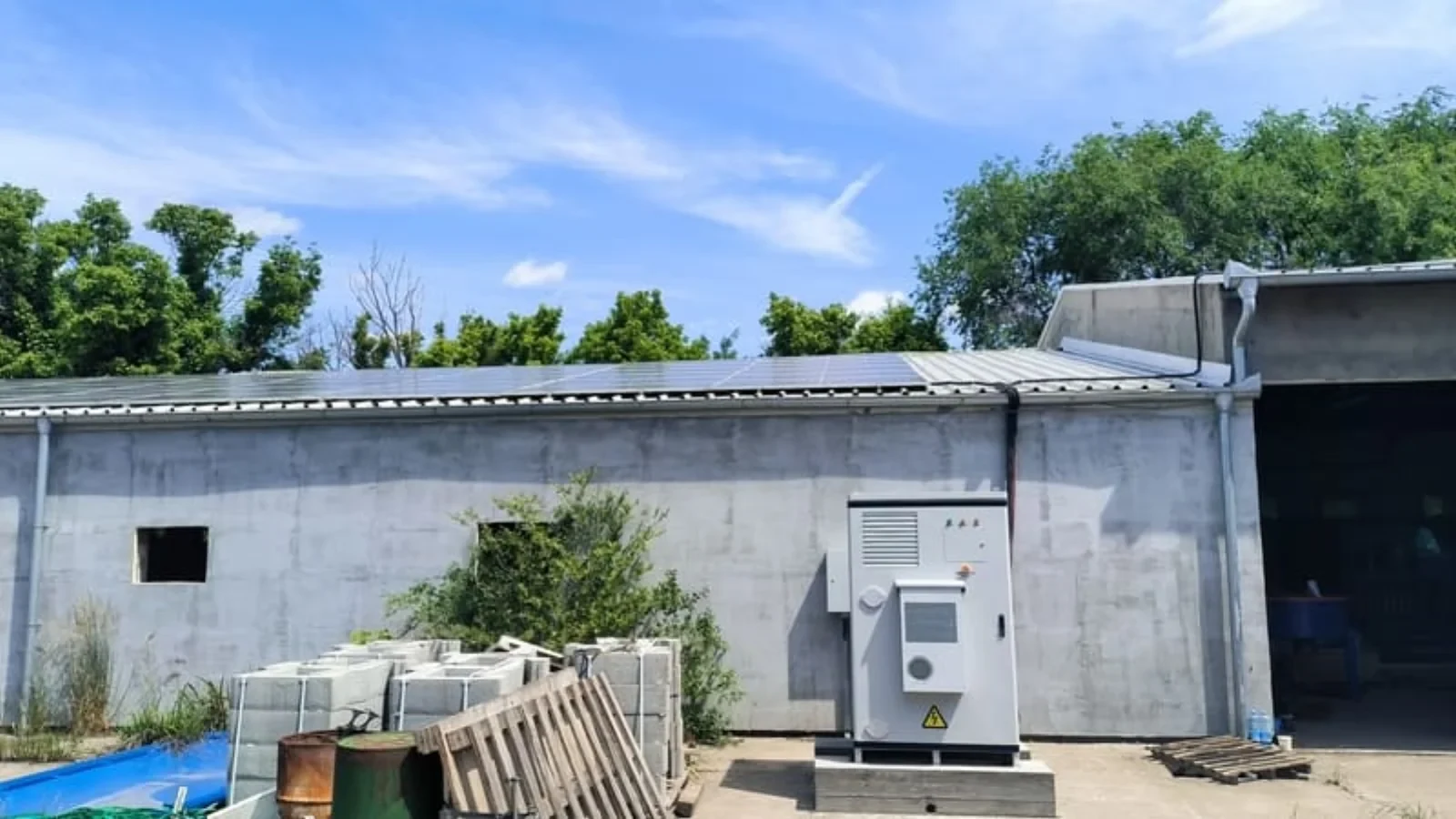 Existing rooftop solar array on a commercial shed with the site's wall-mounted conversion equipment, the side a retrofit has to keep working